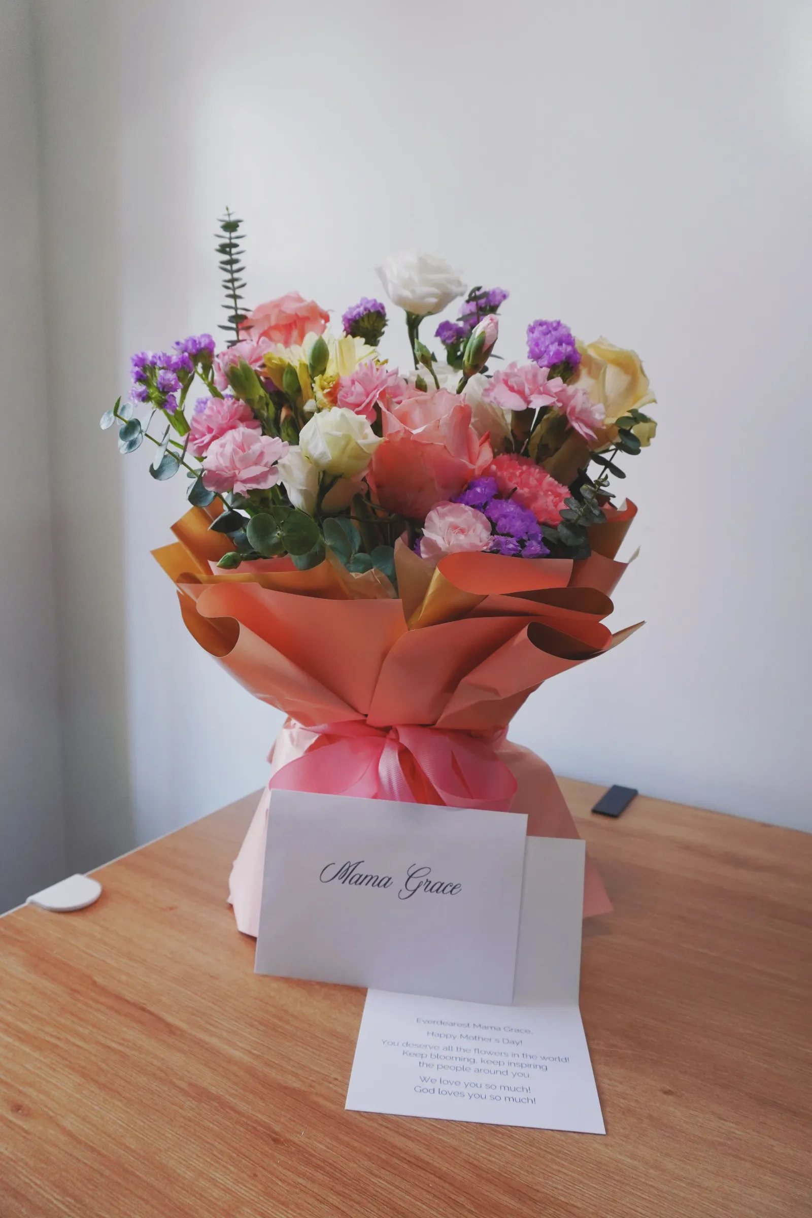 Pink and white Ecuadorian roses, peach China rose, yellow gerbera daisy, light purple statice, pink carnations, and true blue leaves